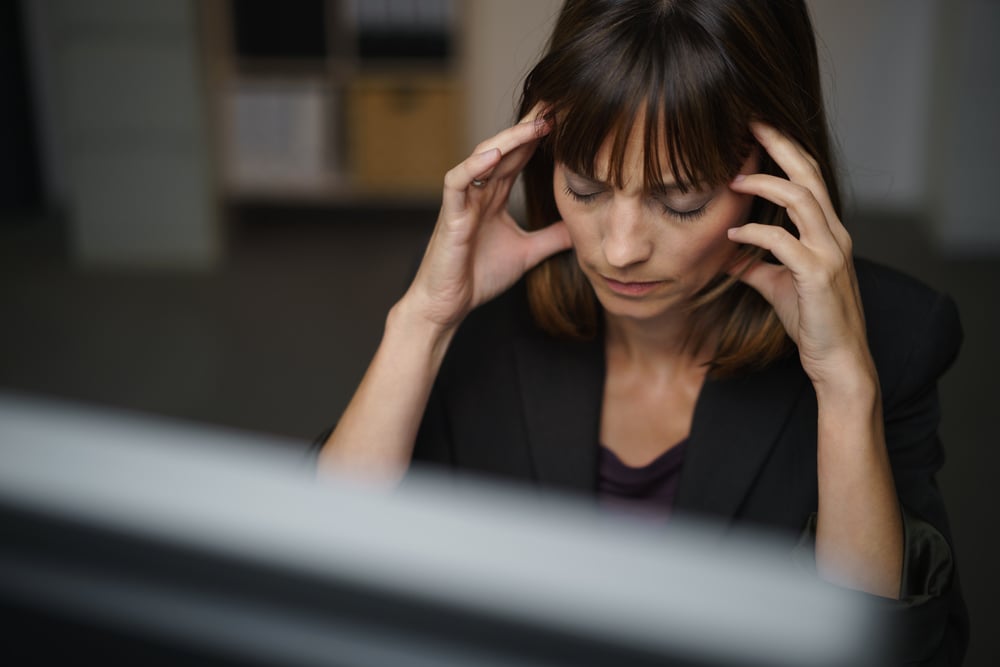 Businesswoman suffering from a headache or migraine holding her hands to her throbbing temples as she works late in the office to a deadline Businesswoman suffering from a headache or migraine holding her hands to her throbbing temples as she works late in the office to a deadline